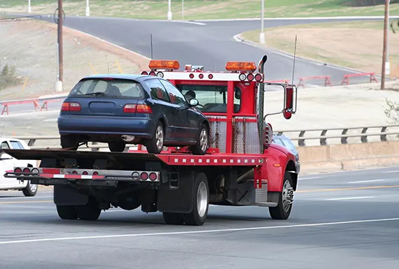 A flatbed tow truck is towing a car, showcasing a typical roadside assistance scenario.