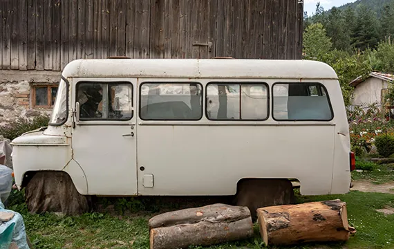 An old white bus parked in front of a barn, symbolizing the need for instant cash for junk cars.