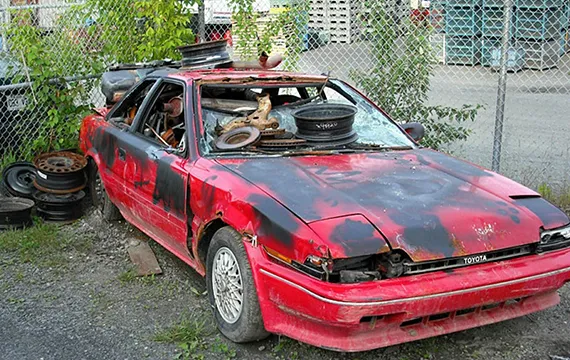 Red car covered in tires and junk for cash offers on junk trucks.