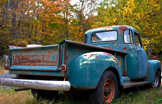 Old blue truck parked in grass symbolizing hassle-free junk car removal services.