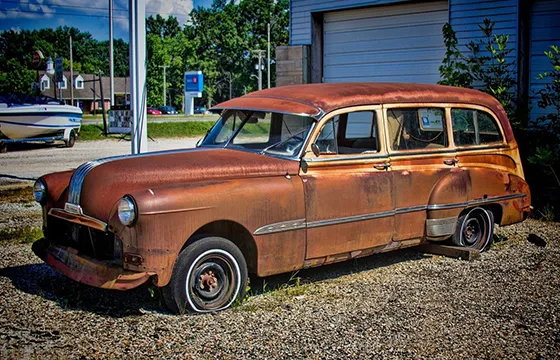 Old rusty car parked in front of a building, illustrating our junk car buying service.
