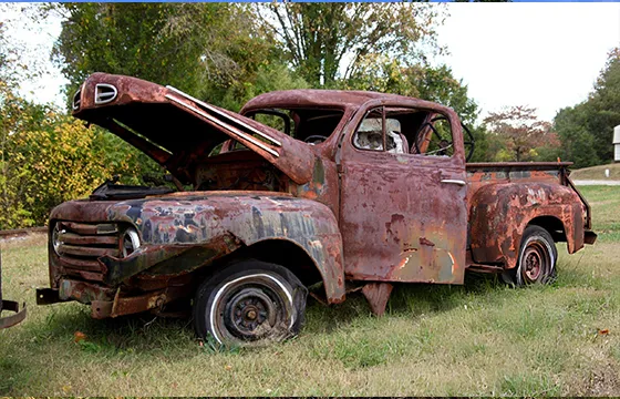Old rusted truck with the hood open, sitting in tall grass, symbolizing junk vehicle services in Grayson, GA.