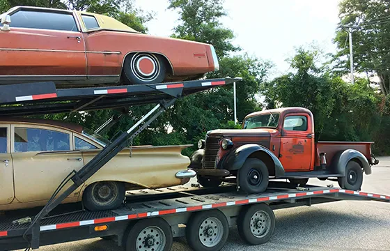 A truck transports an old car and a new car for cash for junk trucks in Lawrenceville GA.