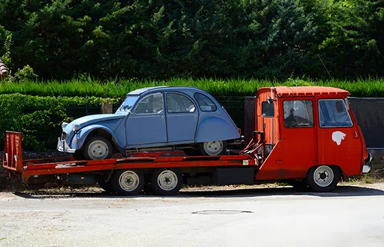 A red truck transports an old car on its flatbed showcasing reliable service and commitment to quality.
