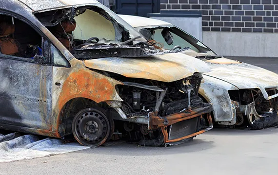 A burnt out van sits in front of a building related to junk car services.