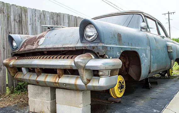 A rusted old car parked in front of a fence symbolizes junk SUVs available for cash.