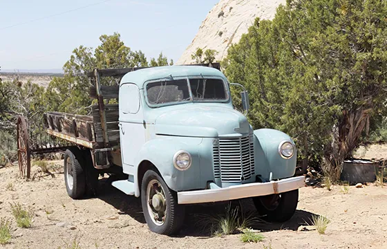 An old truck parked in the desert near a rock wall symbolizes the need for professional junk car removal services.