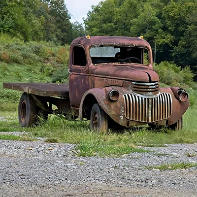 A vintage truck stands still in the middle of a lush green field, surrounded by open space.